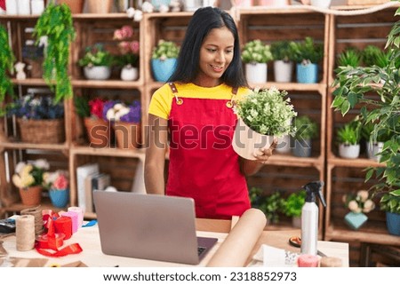 Young beautiful woman florist using laptop holding plant at florist