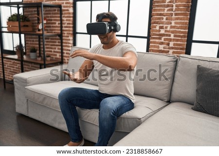 Young hispanic man playing video game using virtual reality glasses at home