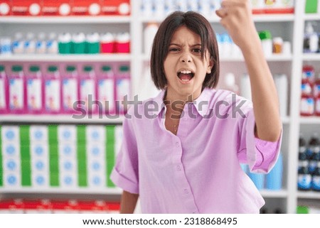 Young girl at pharmacy drugstore angry and mad raising fist frustrated and furious while shouting with anger. rage and aggressive concept.  Royalty-Free Stock Photo #2318868495