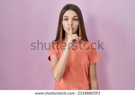 Teenager girl standing over pink background asking to be quiet with finger on lips. silence and secret concept. 
