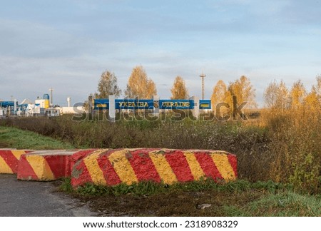 Shield with the inscription Ukraine at the border crossing and a concrete block with red and yellow stripes. TEXT TRANSLATION: UKRAINE