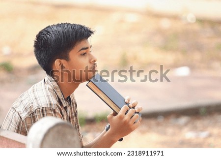 Indian teenage boy reading book in park
