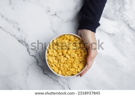Corn flakes in bowl with female hand on marble background.