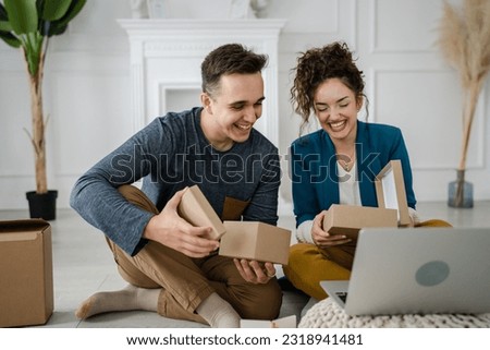 young couple man and woman boyfriend and girlfriend or husband and wife exchange gifts at home giving presents to each other and opening box happy smile celebrate valentine holiday or birthday