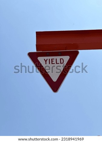 Red and white yield triangle sign posted high on beam with sky in background