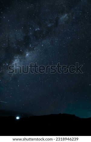 Milky Way filling the portrait frame, shillouetted hills in the dark new moon sky,little house litter beaming towards the stars in the new zealand sky 