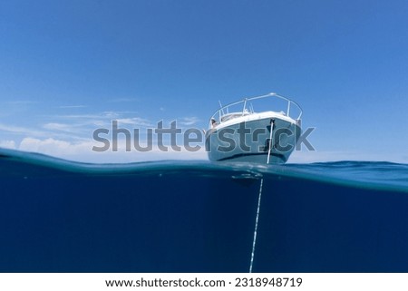 luxury boat sitting on anchor floating in deep blue water with blue sunny skies in background. Split shot of the bow and anchor line of luxury boat as it floats in the ocean in the Bahamas. Royalty-Free Stock Photo #2318948719
