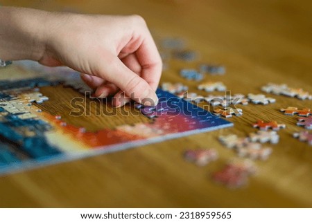 Close-up on woman hand playing puzzles at home. Connecting jigsaw puzzle pieces in a living room table, assembling a jigsaw puzzle. Fun family leisure.