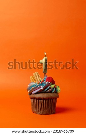 cupcake on orange background with birthday candles - birthday cake with number 1 Royalty-Free Stock Photo #2318966709