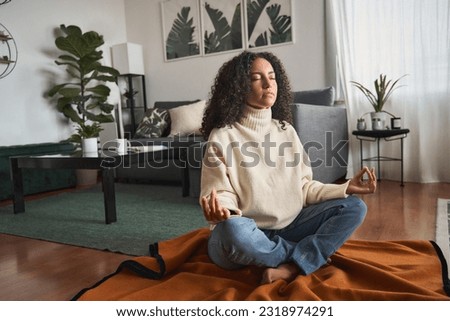 Young calm latin woman doing yoga exercise at home feeling zen. Mindful girl sitting on floor meditating chilling with eyes closed, relaxing breathing for good mental balance, peace of mind. Royalty-Free Stock Photo #2318974291