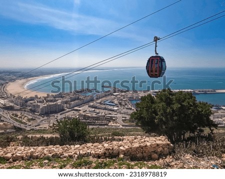 Midway view from Agadir Oufla climb, capturing Agadir's cityscape, Atlantic beach and cable cars under the sunny sky