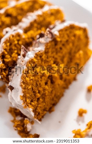 Sliced homemade pumpkin bread with a white glaze and pecans on a white serving tray.