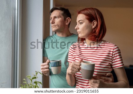 Upset girl and man hold cup of coffee, look out window, sad and anxious. Family problems. Unhappy husband and wife hustle about life and problem solving. Feelings loneliness in couple