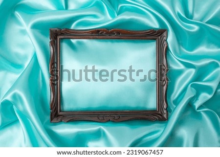 Beautiful blue green silky satin. Soft folds of shiny cloth and vintage wooden frame. Luxury turquoise background with copy space for design. Web banner
