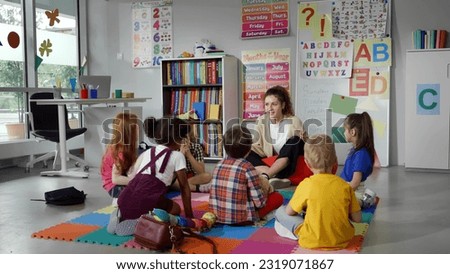 Small nursery school children with teacher sitting on floor having lesson. Young woman teach preschool kids in classroom sitting on floor together Royalty-Free Stock Photo #2319071867