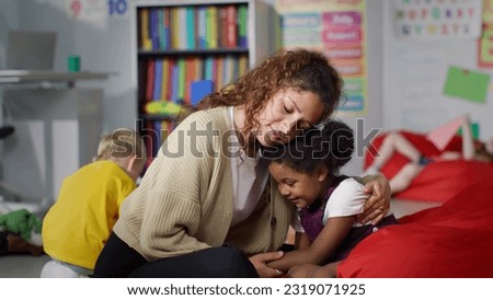 Young teacher cheering and calming upset African-American girl in kindergarten. Female teacher hug and comfort sad kid in nursery school Royalty-Free Stock Photo #2319071925
