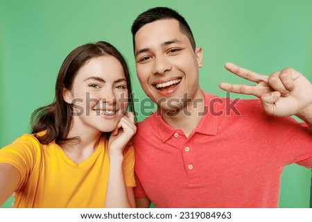Close up young happy couple two friends family man woman wear basic t-shirts together do selfie shot pov on mobile cell phone show v-sign gesture isolated on pastel plain light green color background