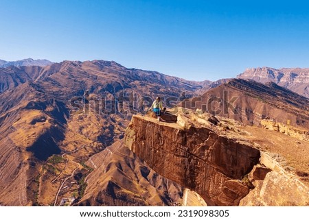 Girl tourist on an extreme ledge in the rock Troll tongue. View of the Caucasus Range, Dagestan. Royalty-Free Stock Photo #2319098305