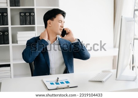 Overworked Asian businessman office worker suffering from neck pain after had a long day at her office desk. office syndrome concept