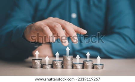 Investor, Trader or Businessman hand control stacking coins at different heights with percentage and arrow icons for interest rating from each investment, Financial profit return and dividend concept.