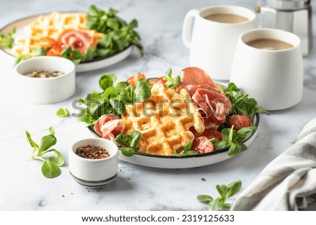 Cheesy belgian waffles served with ham, tomatoes and lettuce corn with cutlery on white marble background. Savory waffles. Healthy breakfast. Horisontal Royalty-Free Stock Photo #2319125633