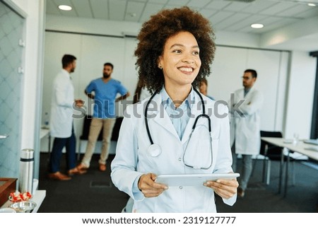 Portrait of a young confident and friendly female black doctor holding tablet computer in fron of group of doctors and nurses. Teamwork and healthcare concept Royalty-Free Stock Photo #2319127777