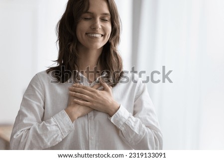 Close up portrait happy attractive young woman holding folded palms on chest with closed eyes, express gratitude, believe, faith, charity. Sincere volunteer show devotion, kindness, feel appreciation
