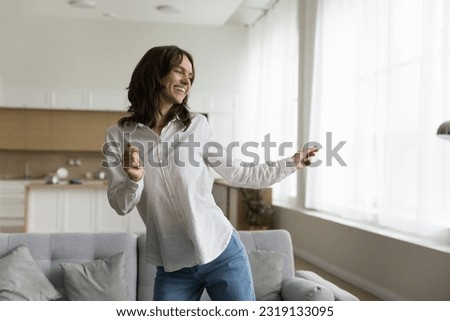 Untroubled woman tenant or home-owner dancing in cozy studio apartment, spend leisure indoor, moving to favourite music, having day-off in living room. Hobby, active pastime, vitality. Enjoy your life Royalty-Free Stock Photo #2319133095