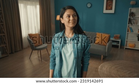 Young smiling Asian woman in a clean bright living room. A young woman looks around the room with a satisfied smile. Royalty-Free Stock Photo #2319142691