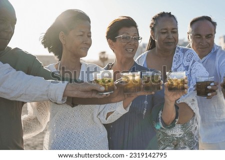 Multiracial senior friends cheering with mojitos drinks on the beach - Elderly people having fun together during travel vacation - Focus on the asian woman face