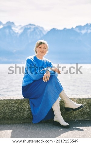 Outdoor fashion portrait of happy mature woman posing by the lake, wearing blue  pullover and skirt