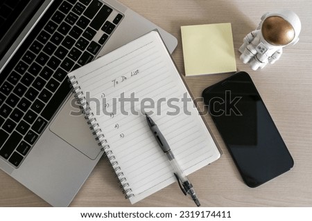 Top view of workplace with to do list on notepad, ballpoint pen, some sticky notes, a laptop and smartphone, astronaut figurine on wooden desk. Organization and to do list concept. Royalty-Free Stock Photo #2319174411