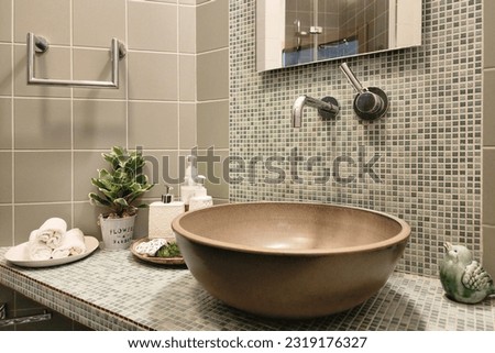 Stylish bathroom design. Modern sink bowl on the countertop decorated with mosaic tiles. Hygiene products, towels, potted houseplant. Royalty-Free Stock Photo #2319176327