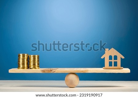 Property investment and house mortgage financial real estate concept. Wooden home and money coins stack on wood scale.