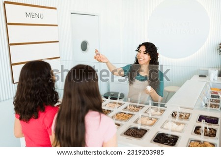 Woman worker selling ice cream or frozen yogurt with delicious toppings to teenage girl customers at the shop Royalty-Free Stock Photo #2319203985