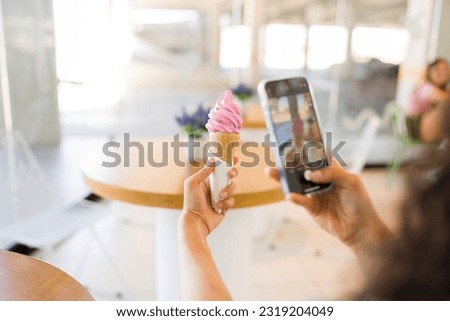 Close up of a young woman seen from behind taking a picture of her delicious strawberry ice cream cone with her smartphone