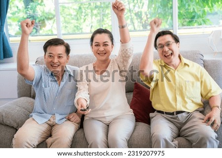 Happy senior friends watching TV and cheer up sitting on sofa cozy room look from forward view
