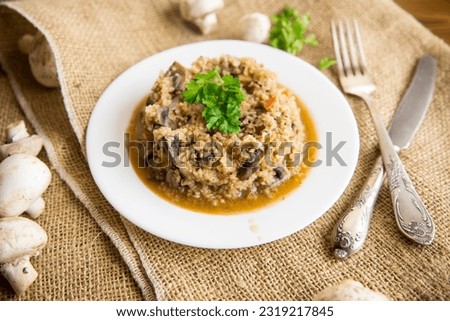 cooked bulgur with mushrooms, carrots and vegetables in a plate, on a wooden table.