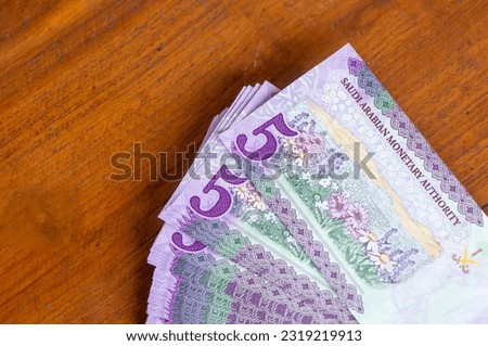 A pile of Saudi Arabia five riyals banknotes money on wooden table, selected focus