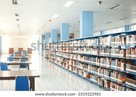 Inside a modern library with many books on book shelves, empty chairs and tables, diminishing perspective and shallow dof