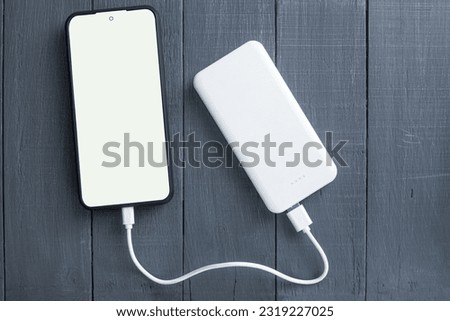 Phone and power bank, on a wooden background. Copy space. White power bank and smartphone on a wooden background. White phone screen with space for text Royalty-Free Stock Photo #2319227025