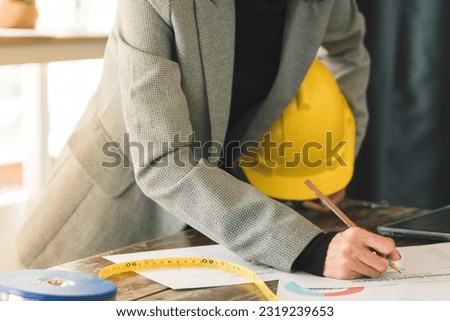 Close-up of Engineer holding helmet checking accuracy of building structural blueprints from architect on the desk in office to proceed with the construction, engineer and construction concept