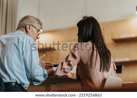 A back view shot of 70s experienced male business person giving advices to his female junior employee for better efficiency at work