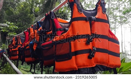 Bright orange marine life vest signal jackets close up hanging on hanger, safety on water tourism activity and watersports Royalty-Free Stock Photo #2319265005