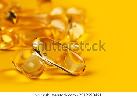 twoo capsules Omega 3 on yellow background and many other of capsules on blurred background. Health care concept.