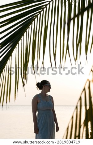 Pretty woman enjoy sunset near the ocean. Tropical island. Lot of palm leaves 