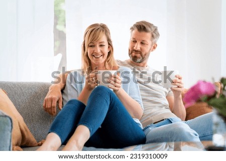 Portrait of smiling woman drinking tea with boyfriend. Mid aged couple is spending leisure time together. They are sitting on sofa at home.