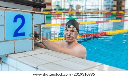 Fit strong swimmer with a black swimming cap looking at the pool, deep focusing on the race with swimming goggles. Royalty-Free Stock Photo #2319310995
