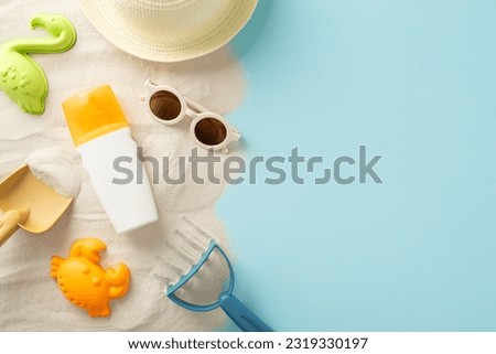 Beach activities for children concept. High angle view picture capturing sunhat, sunglasses and sunscreen bottle with sand molds and seashells on the sand on isolated blue backdrop offering copyspace Royalty-Free Stock Photo #2319330197