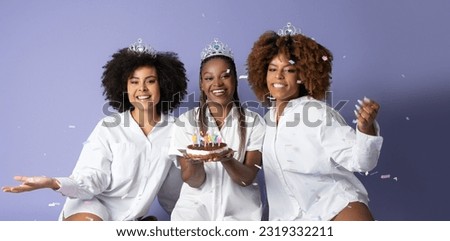 Birthday Party Celebration. Three Happy Black Ladies Holding Bday Cake With Burning Candles, Posing With Falling Silver Confetti Over Purple Studio Background. Holiday With Friends. Panorama